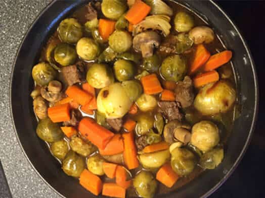 Poêlée de choux de Bruxelles, carottes et champignons cuits avec des morceaux de viande dans une cocotte noire